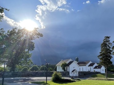 Botne kirke under mørk himmel med solen som titter frem